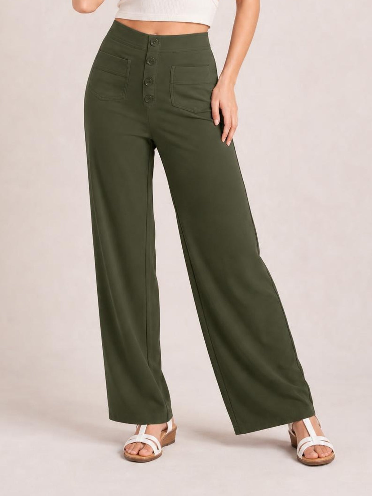 Model wears dark olive high-waist wide-leg pants with front button closure, visible patch pockets, and a relaxed full-length silhouette.