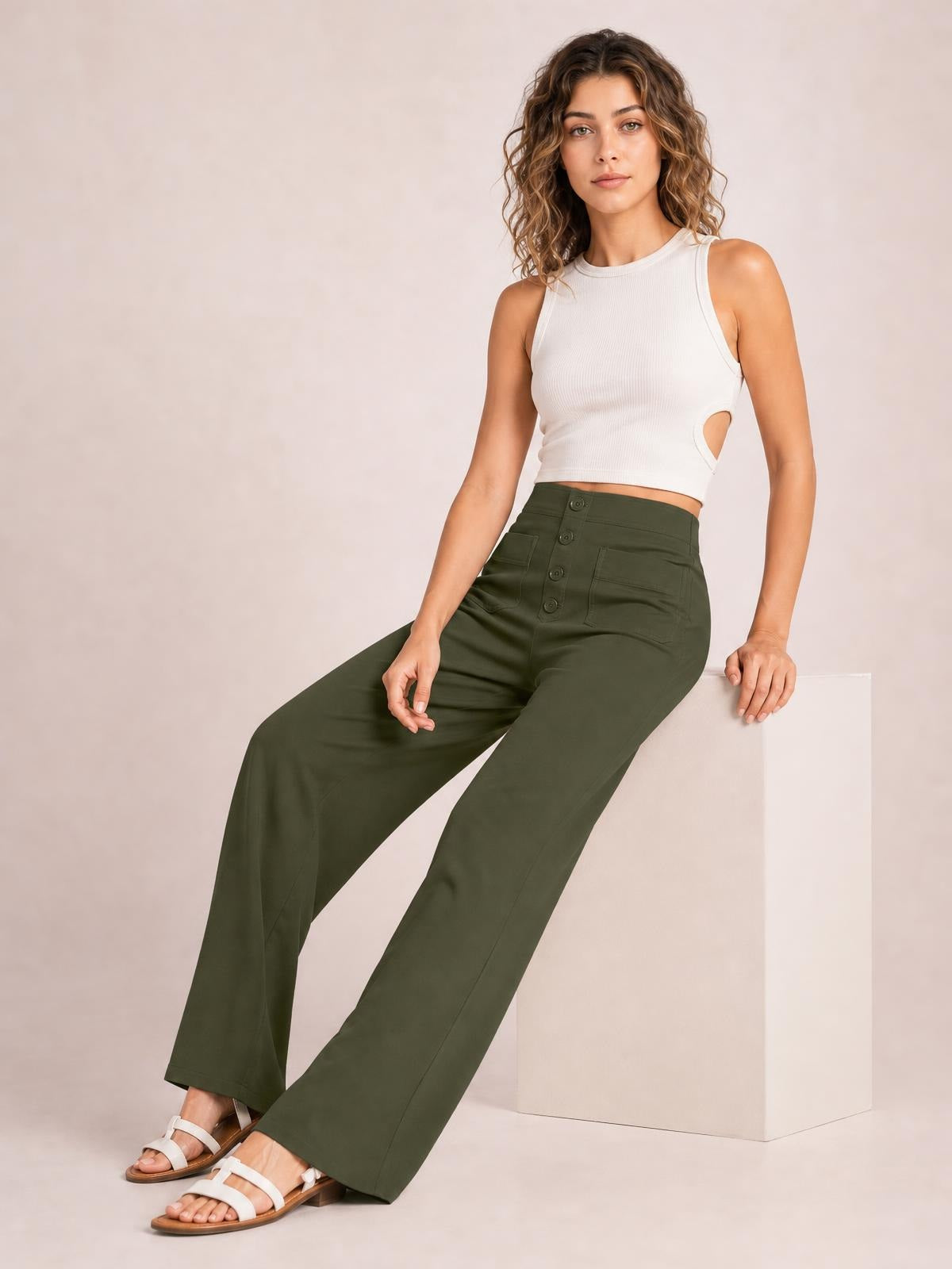 A model sits leaning on a cube, wearing olive green high-waist wide-leg pants with front button details and visible pockets.