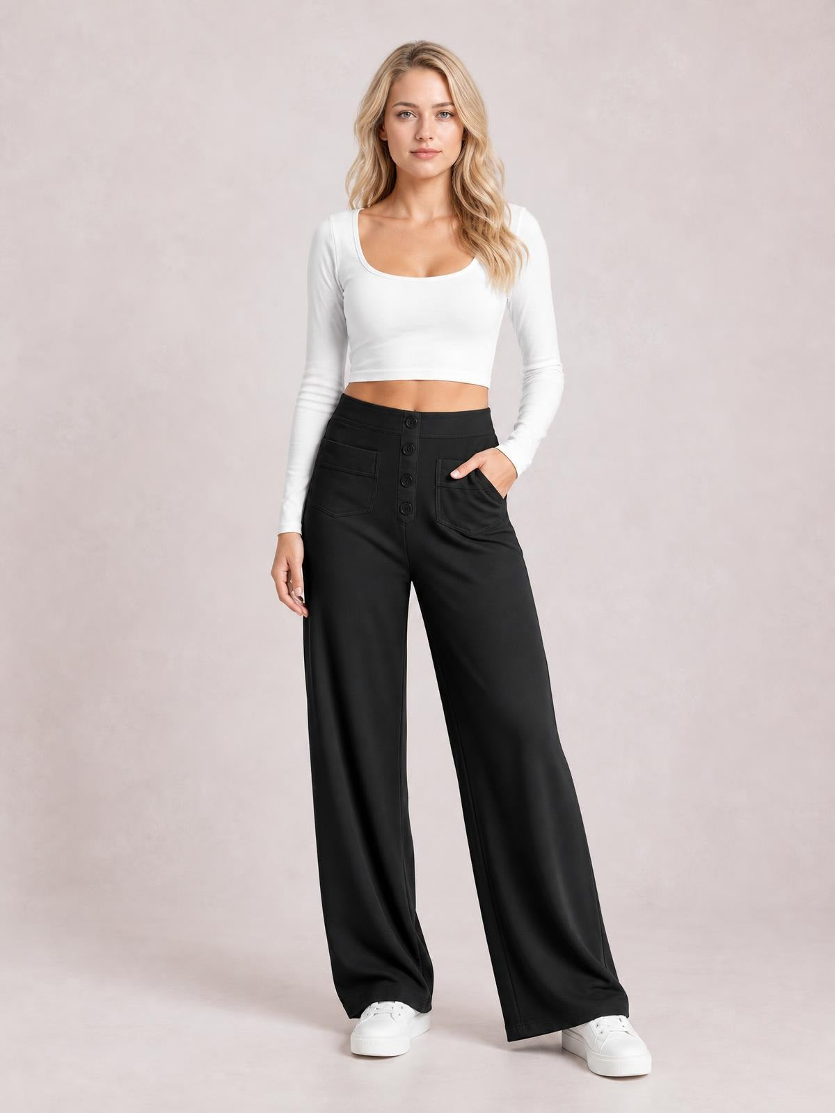 Model wears black high-waist wide-leg pants with front pockets and button fastening, standing with one hand in a pocket.