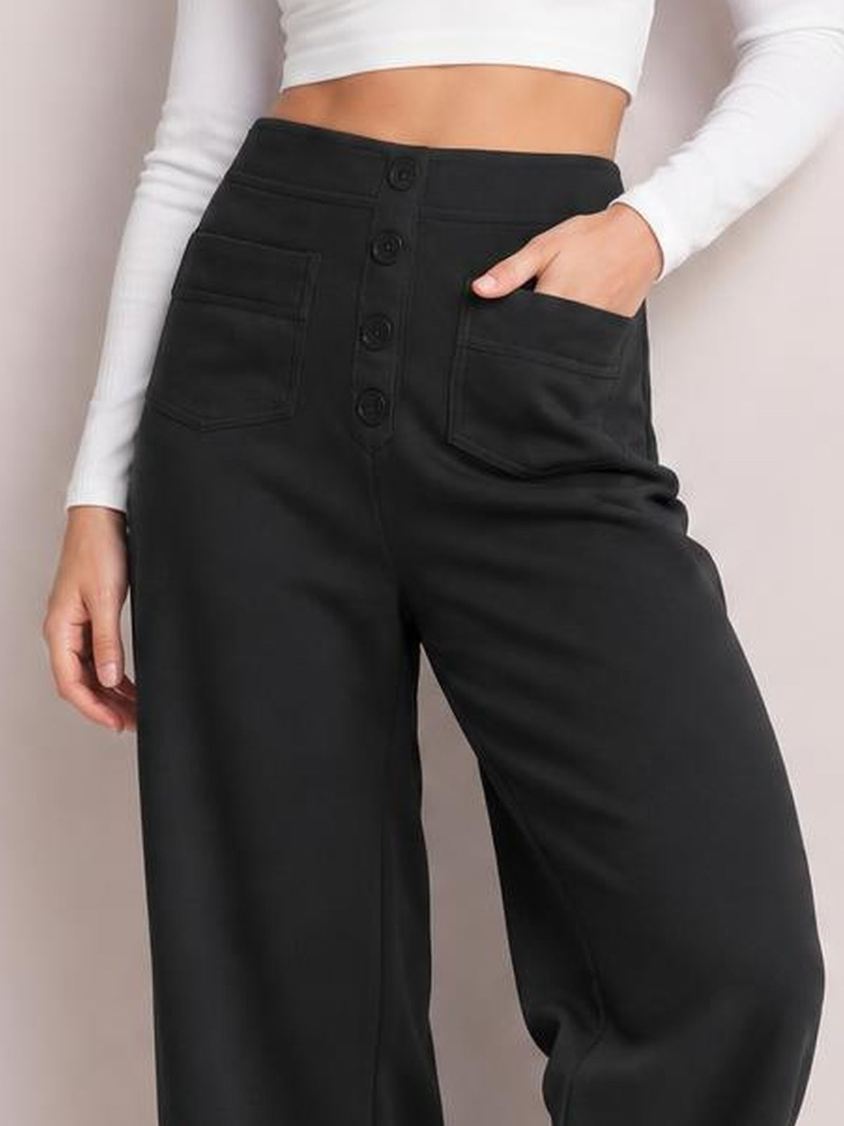 A model poses in black high waist wide leg pants with a button-front closure, oversized patch pockets, and a relaxed, roomy silhouette.