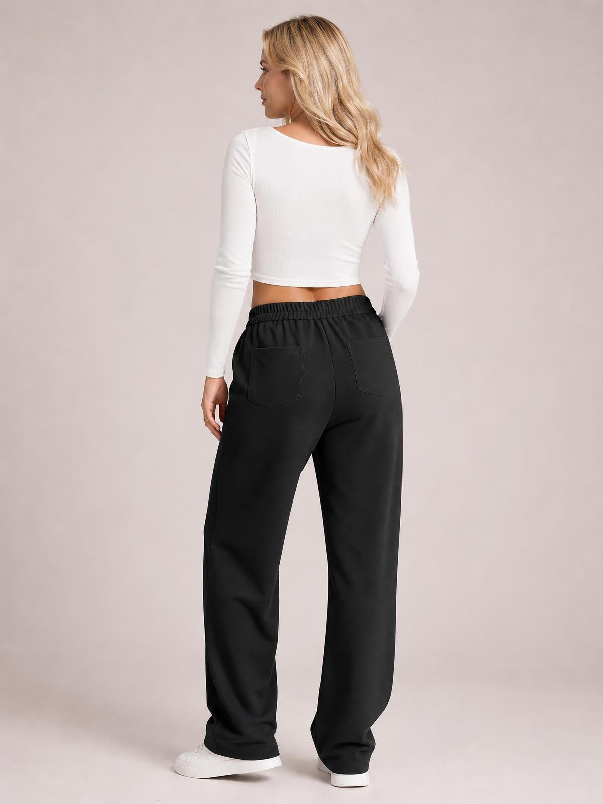 A model poses from the back in black high waist wide leg pants with an elastic waistband and two visible back pockets.