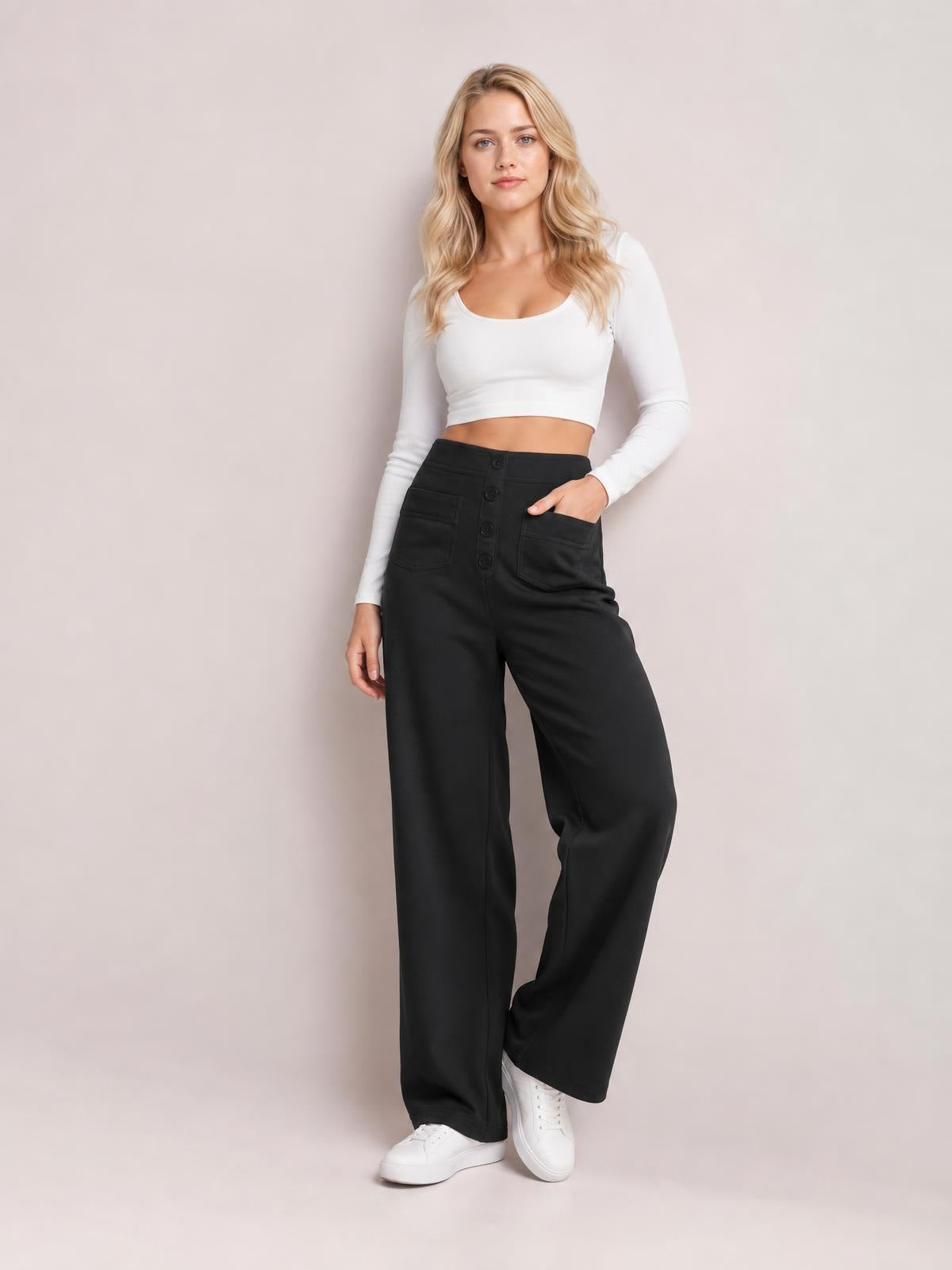 A model poses in black high waist wide leg pants with front button closure and patch pockets, standing with one hand in a pocket.