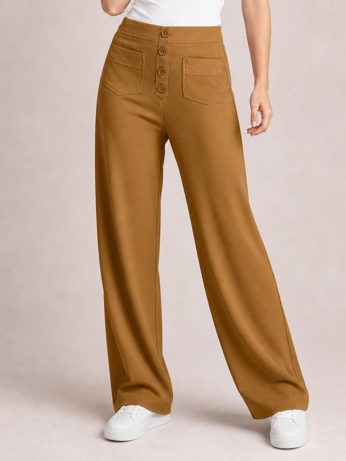 Model wears camel-brown high-waisted wide-leg pants with front patch pockets, belt loops, and a button placket, standing in a relaxed pose.