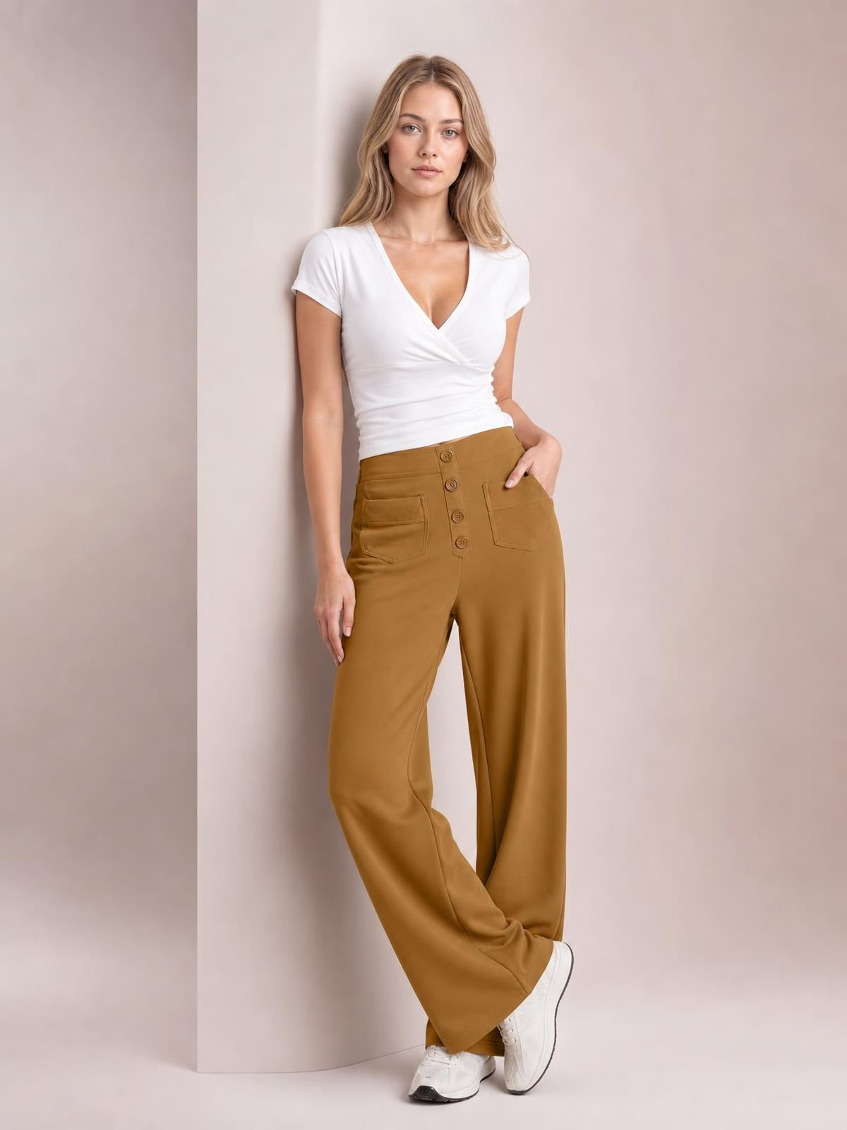 Model poses with one hand in the pocket wearing camel high-waist wide-leg pants with front pockets, a button-front closure, and a flowing silhouette.
