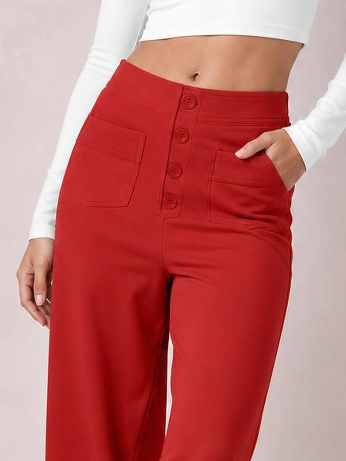 A cropped model wears bright red high-waist wide-leg pants with front button closure, stitched pockets, and one hand tucked into a pocket.