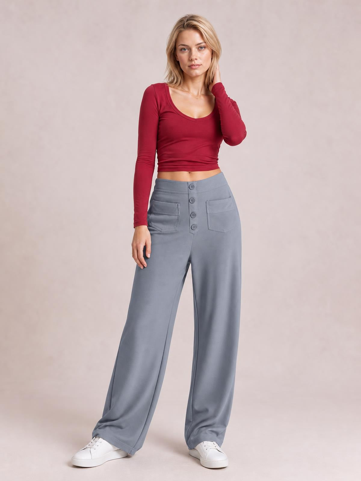 Model poses in gray high-waist wide-leg pants with front button closure, stitched pockets, and a flowing full-length silhouette.