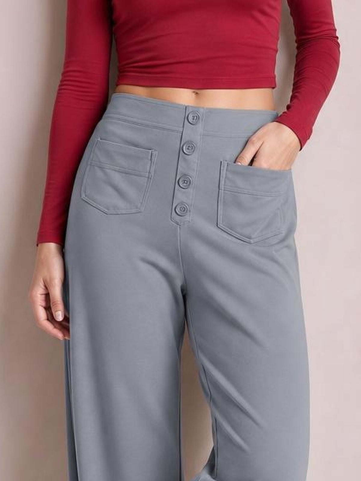 Model wears gray high-waist wide-leg pants with front button closure, stitched patch pockets, and one hand resting in a pocket.