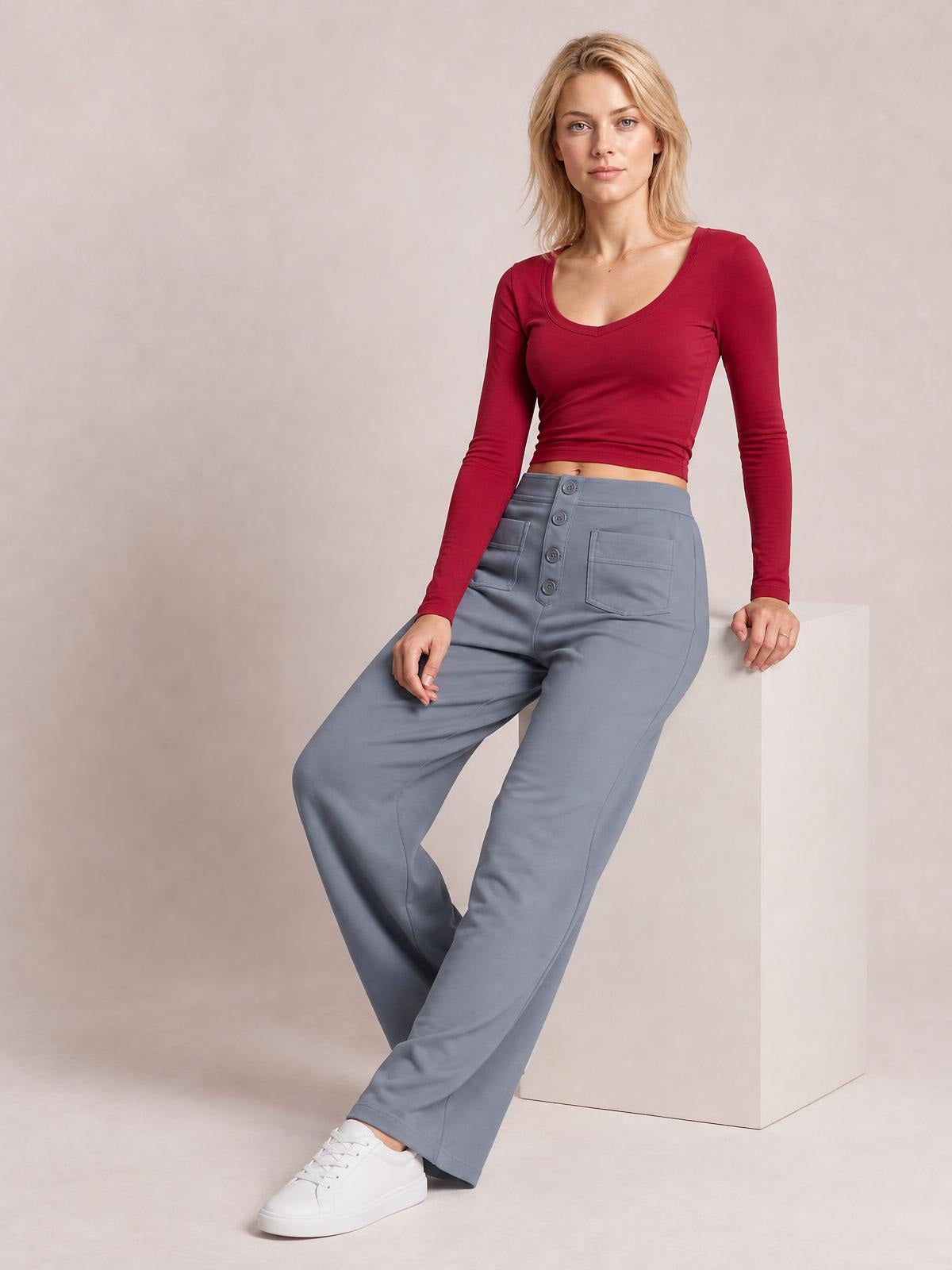 Model poses seated in gray high waist wide leg pants with front pockets, button fly, and a relaxed silhouette.