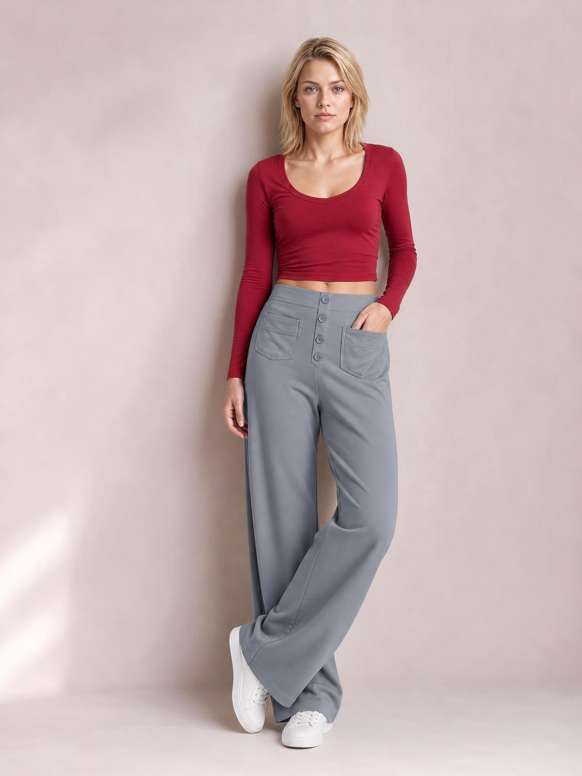 A model poses with one hand in the pocket of gray high-waist wide-leg pants, featuring front patch pockets and a visible button-fly closure.