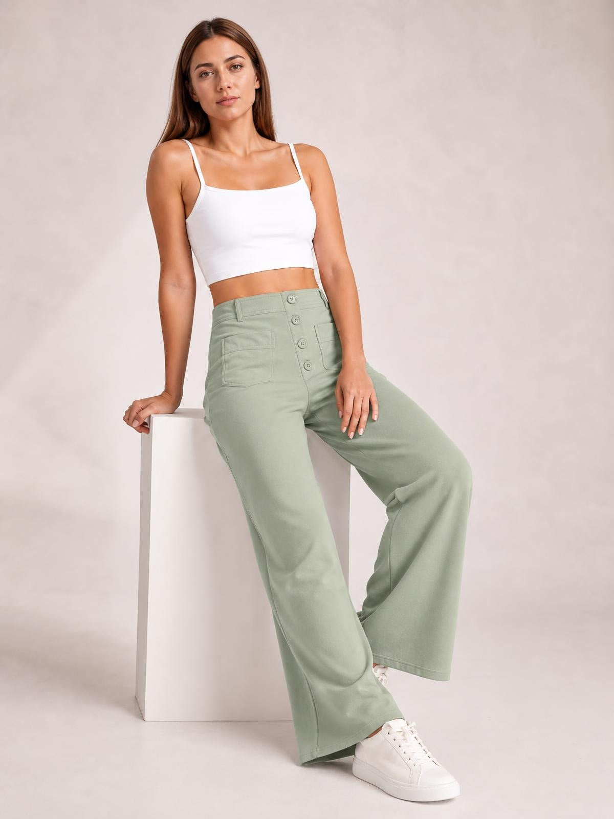 A model poses in sage green high waist wide leg pants with front pockets and a button-fly closure, styled with a white cropped camisole.