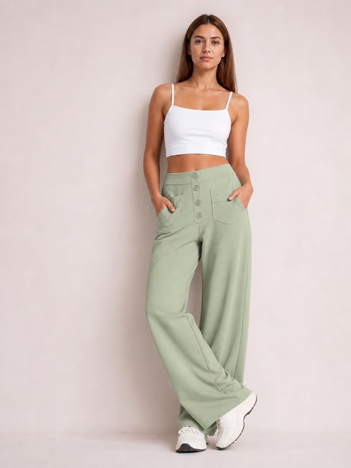 Model poses with crossed legs and hands in the pockets of sage green high-waist wide-leg pants featuring a button fly and relaxed silhouette.