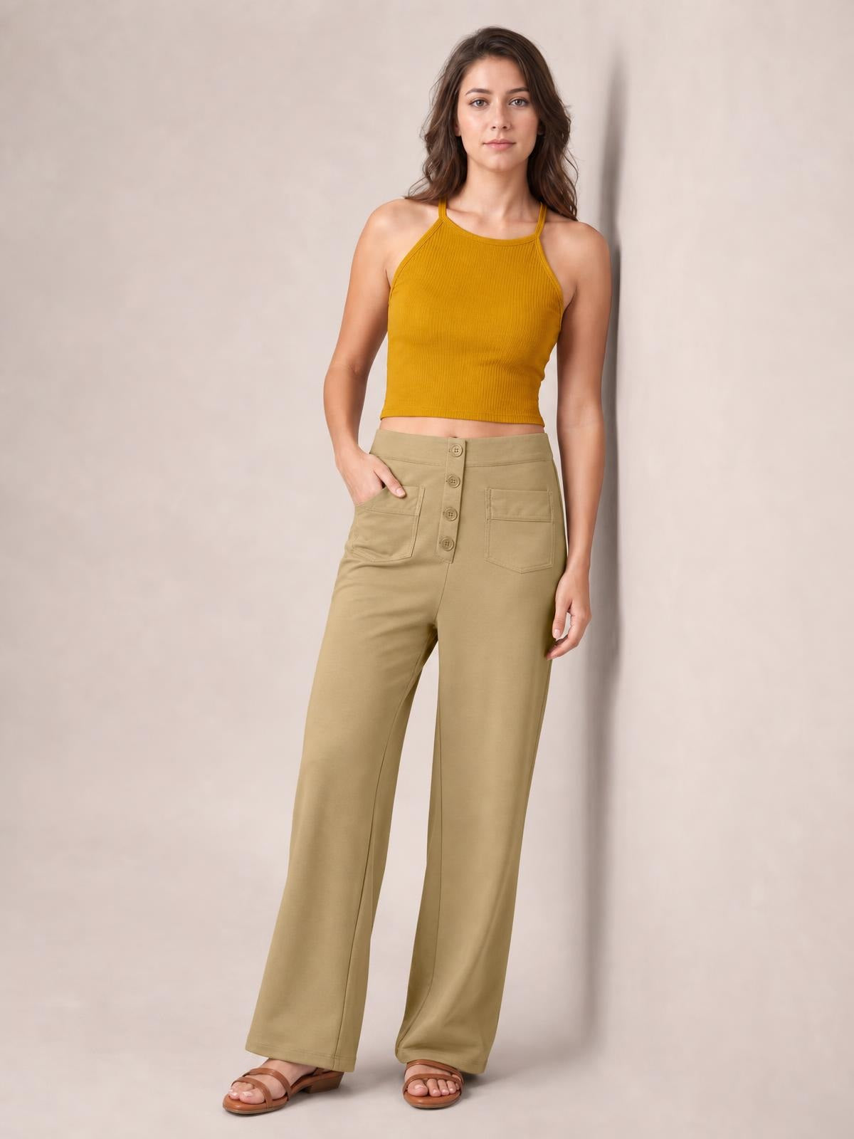A model poses in khaki high-waist wide-leg pants with a relaxed silhouette, front button closure, and two large patch pockets, one hand tucked inside.