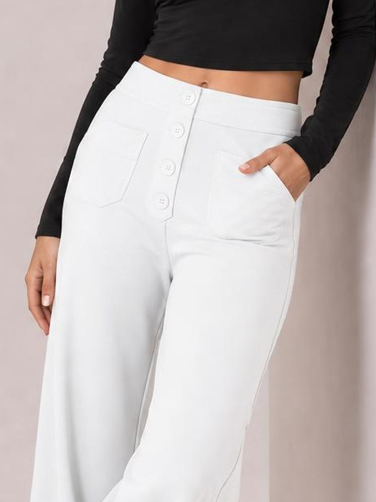 A model wears opaque white high-waist wide-leg pants with a front button fly and pockets, standing with one hand tucked into a pocket.