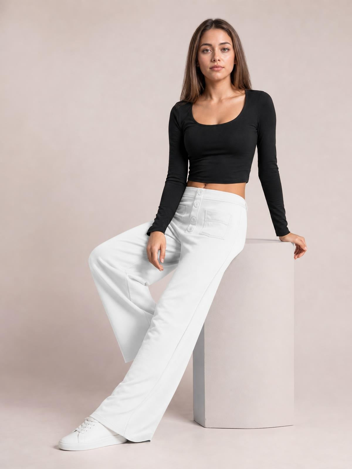 Model seated in white high-waist wide-leg pants with front buttons and patch pockets, styled with a black long-sleeve crop top.