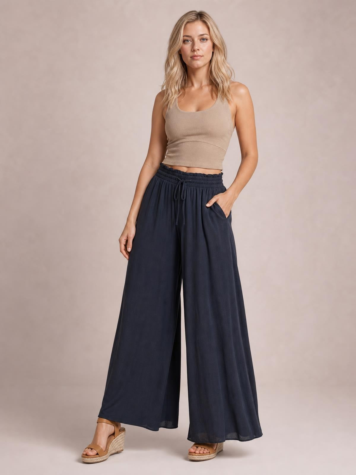 Model poses in navy high waist wide leg pants with an elastic drawstring waistband, flowing full-length silhouette, and practical side pockets.