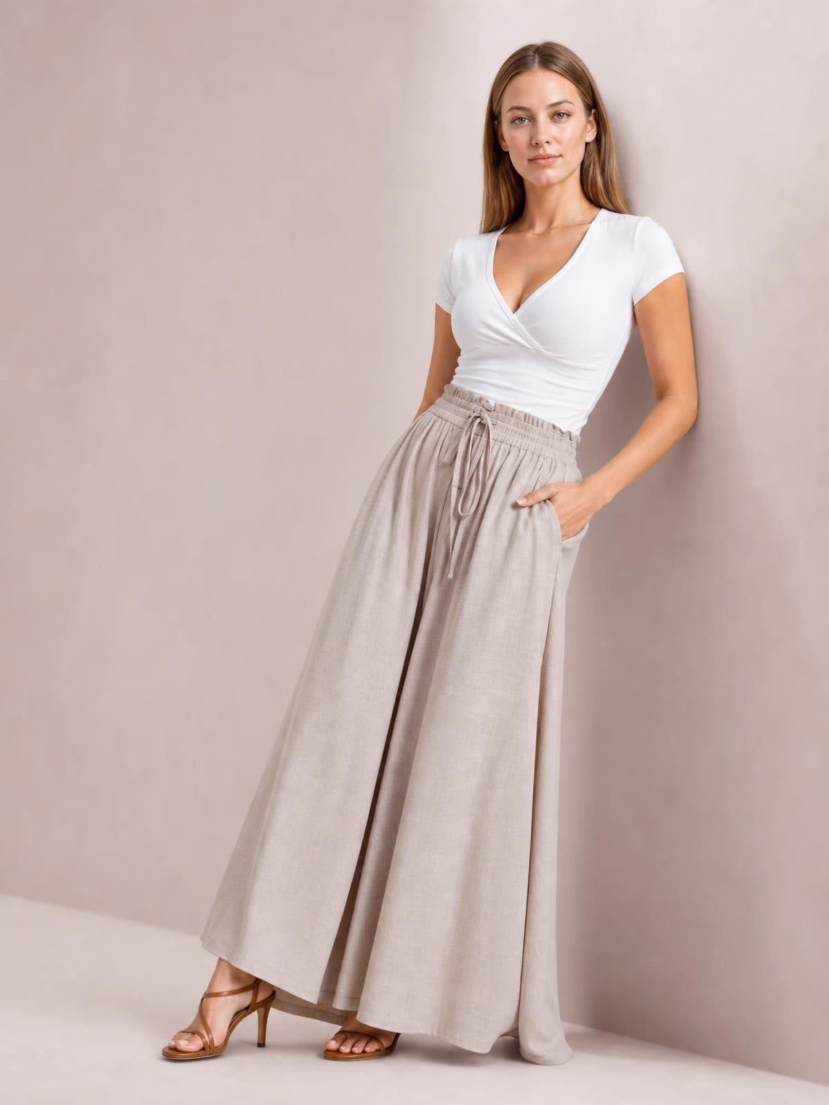 Model poses in beige high waist wide leg pants with a drawstring waistband and practical side pockets, styled with a fitted white top.