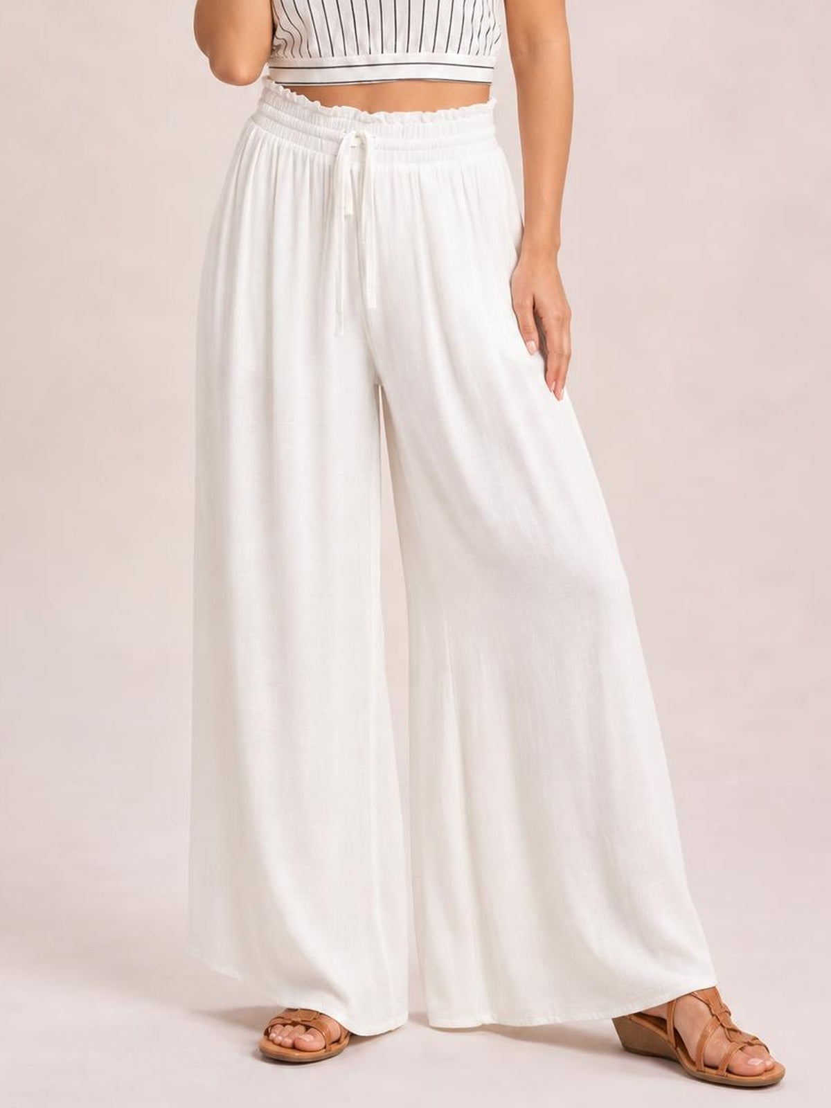 Model wearing white high waist wide leg pants with an elastic waistband, drawstring, relaxed flowing silhouette, and side pockets.
