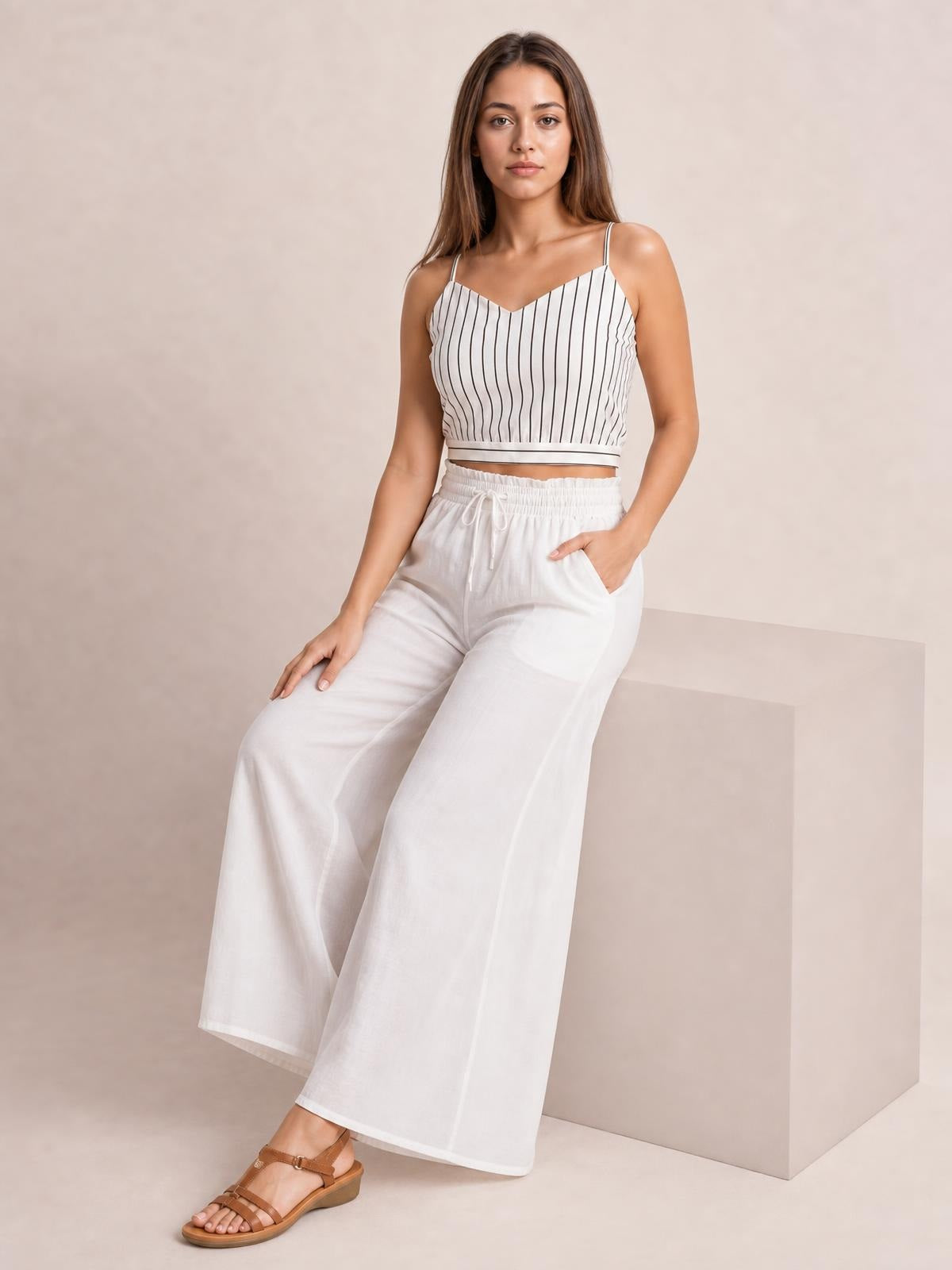 A model sits wearing white high-waist wide-leg pants with an elastic drawstring waistband, flowing silhouette, and practical side pockets.