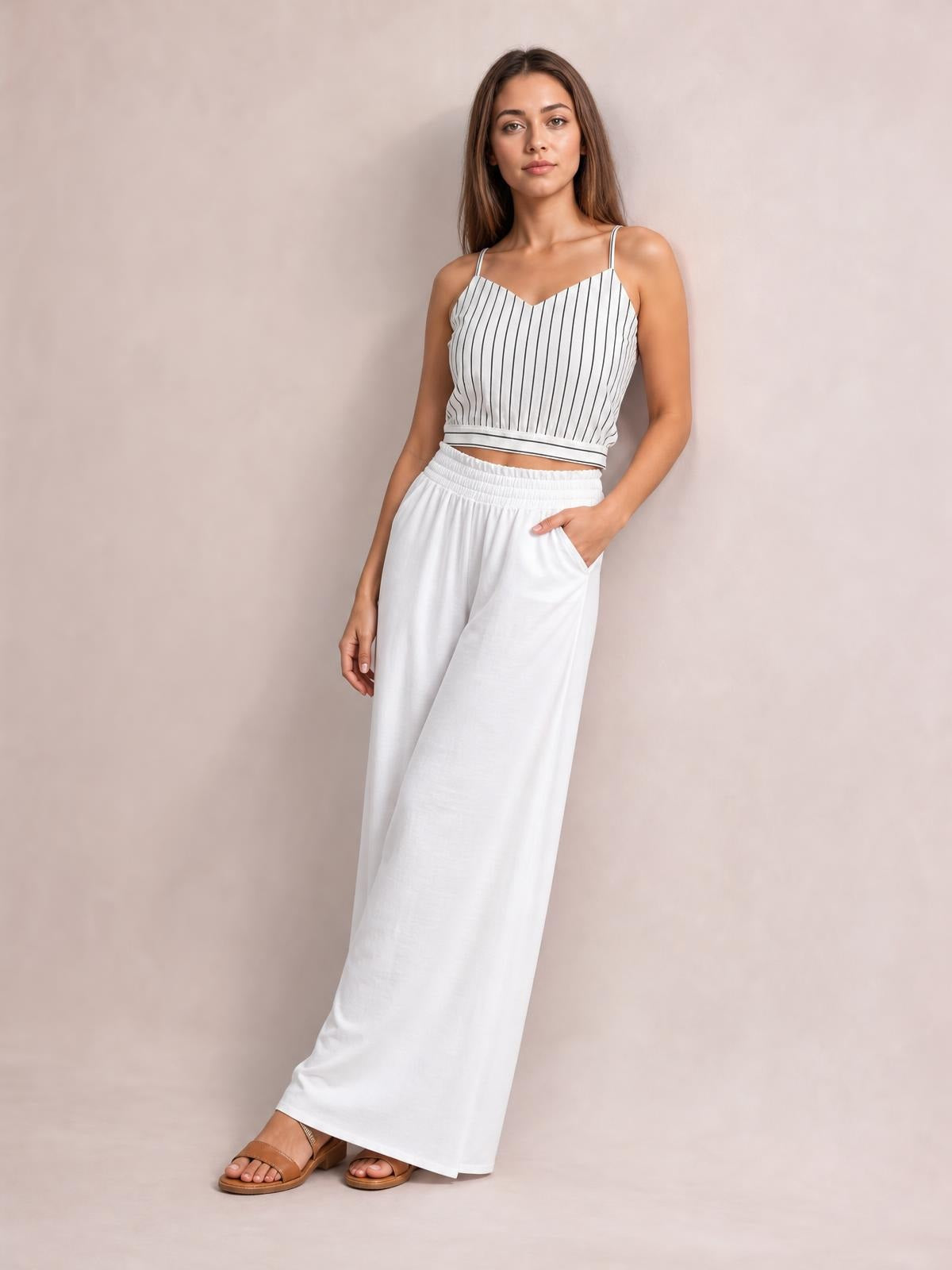 Model wearing white high waist wide leg pants with a relaxed floor-length silhouette and side pockets, posing with one hand tucked into a pocket.
