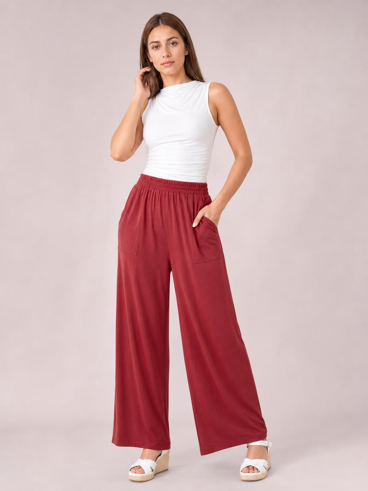Model poses in burgundy high-waist wide-leg pants with an elastic waistband, oversized silhouette, and visible side pockets.