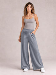 Model poses in gray high-waist wide-leg pants with an elastic waistband and large front pockets, one hand tucked into a pocket.