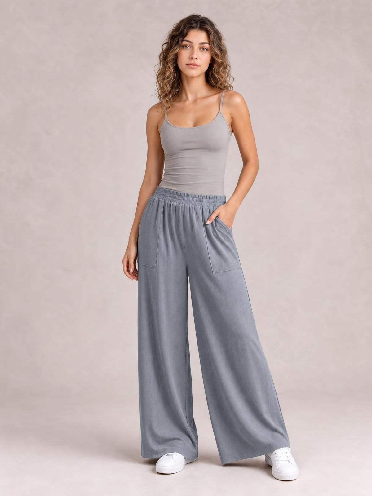 Model poses in gray high-waist wide-leg pants with an elastic waistband and large front pockets, one hand tucked into a pocket.
