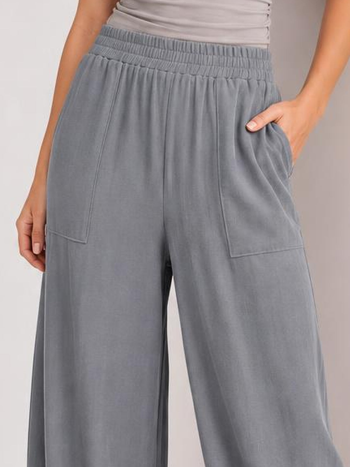 Model shown from waist to legs wearing gray high-waist wide-leg pants with an elastic waistband, roomy silhouette, and large stitched patch pockets.
