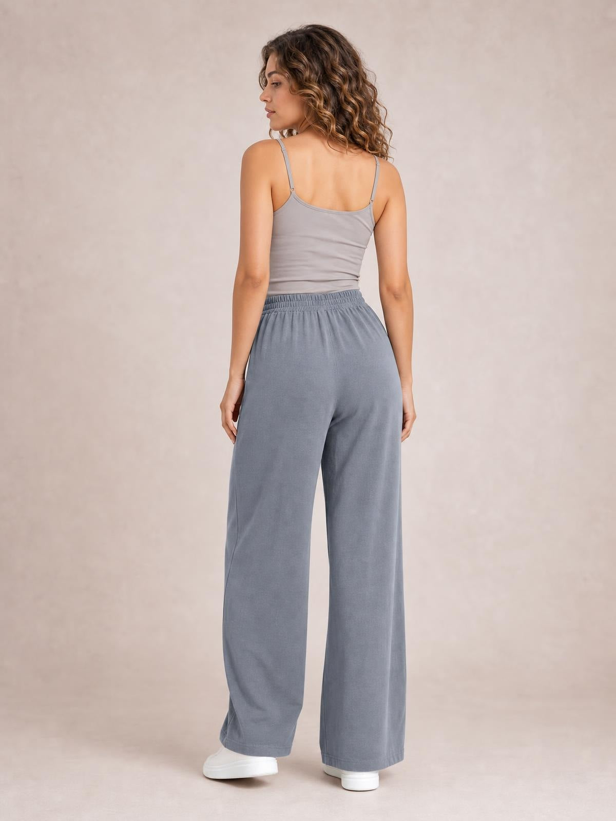 Model poses from the back in gray high-waist wide-leg pants with an elastic waistband, relaxed silhouette, and side pockets.