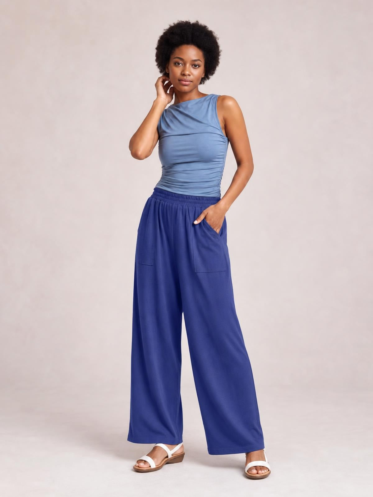 Model poses in blue high-waist wide-leg pants with large front pockets and a relaxed full-length silhouette.
