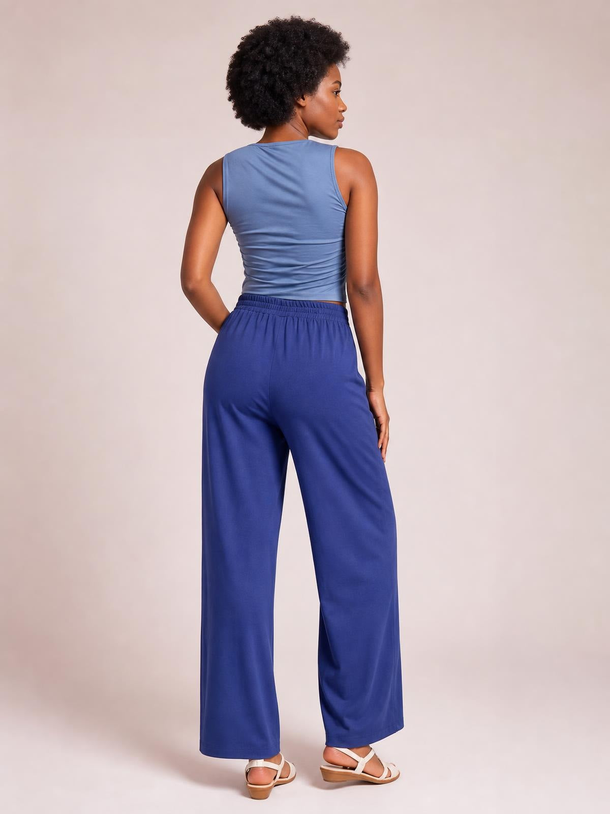 Model turned slightly away displays opaque navy high-waist wide-leg pants with an elastic waistband, relaxed silhouette, and side pockets.