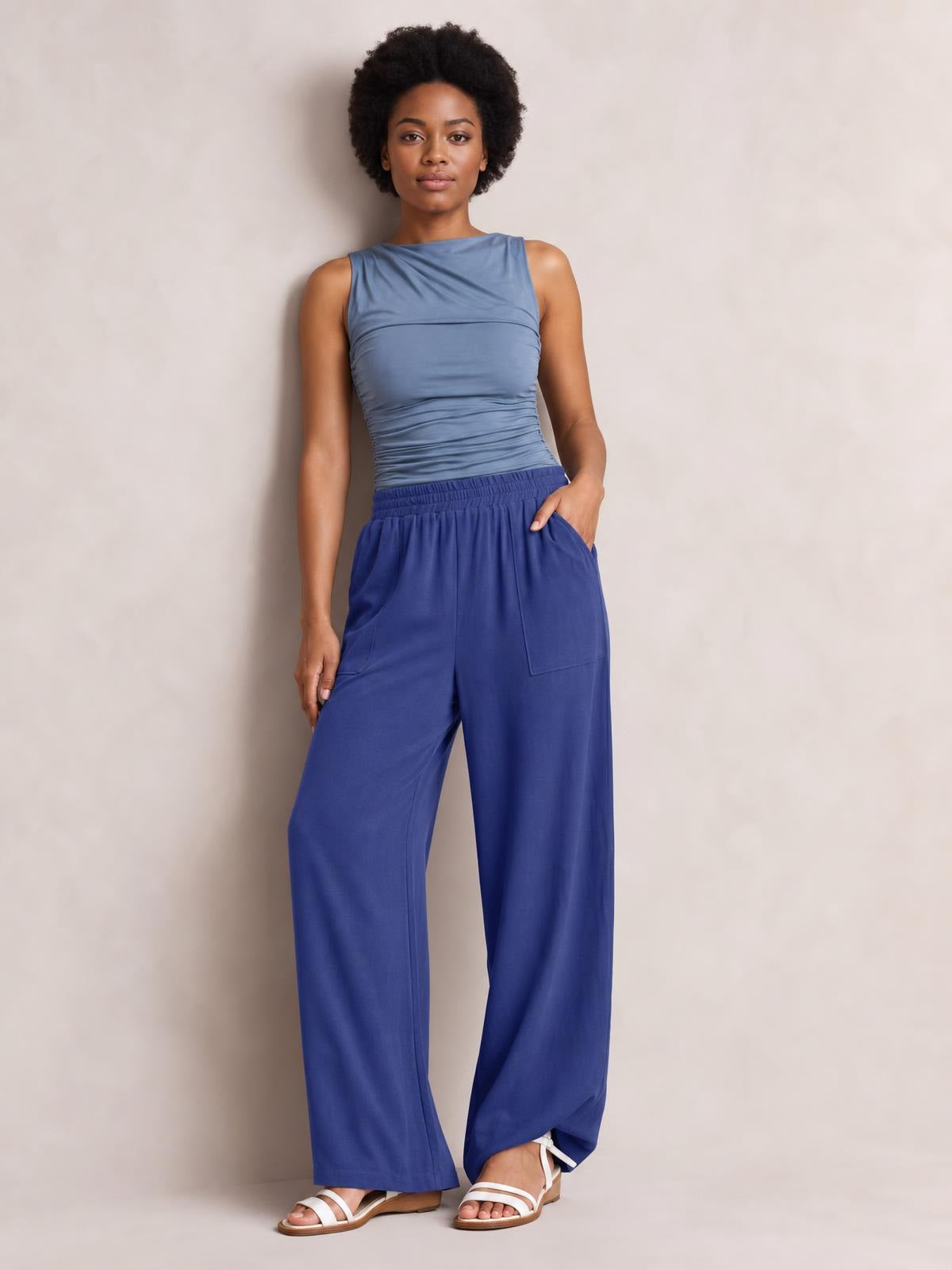 Model poses in blue high-waist wide-leg pants with an elastic waistband and visible front pockets, one hand tucked into a pocket.