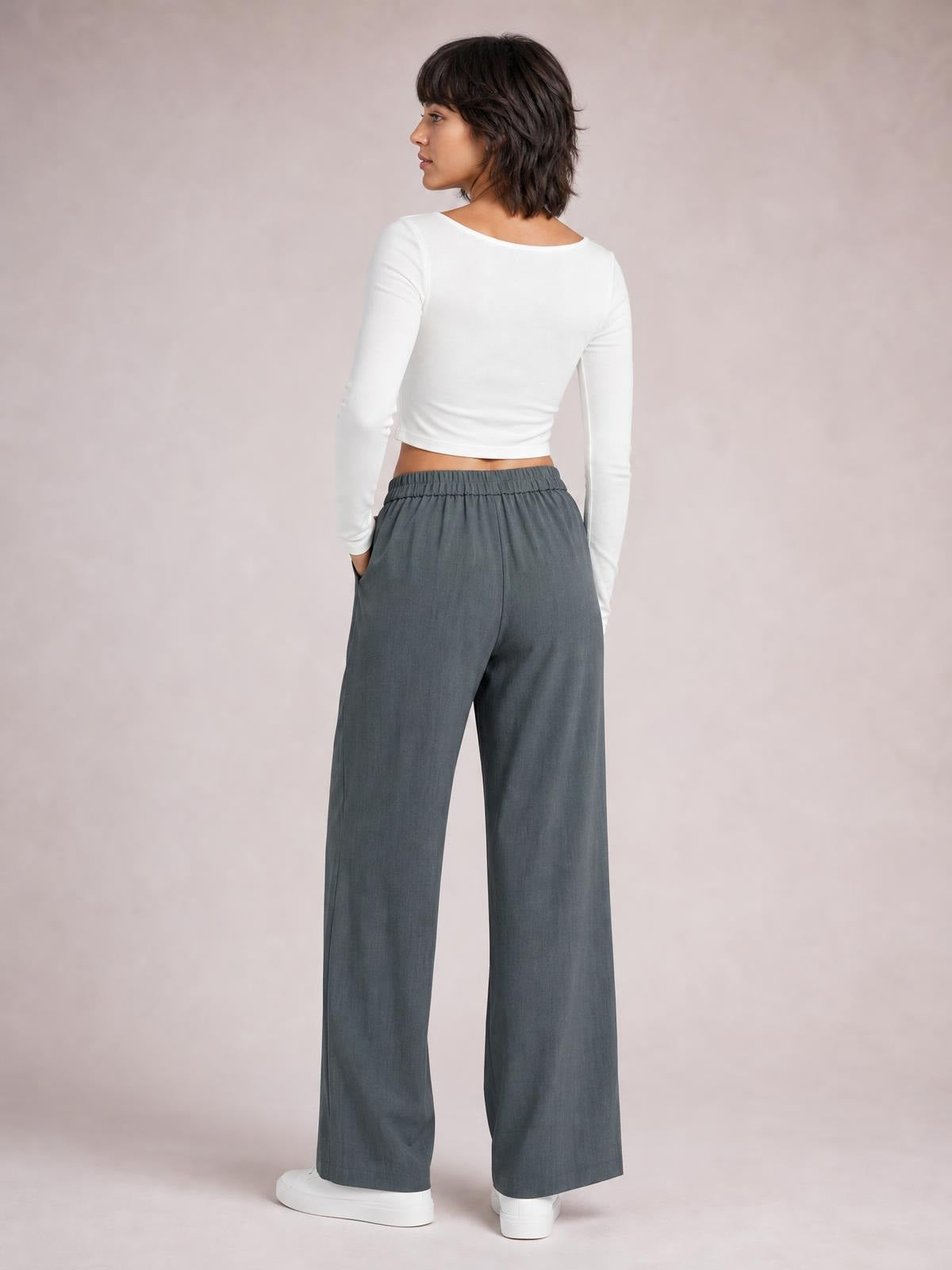 Model shown from behind wearing gray high-waist wide-leg pleated pants with a relaxed silhouette, side pockets, and hands tucked into the pockets.