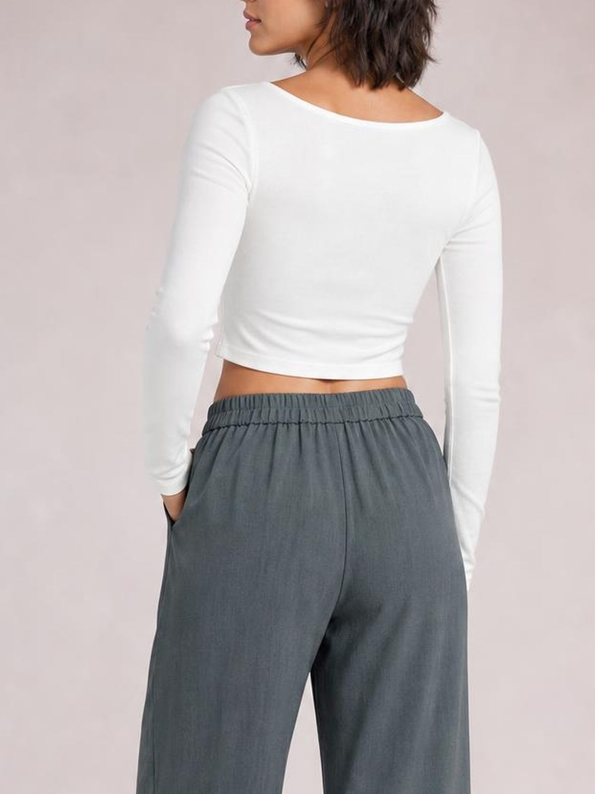 A standing model shows charcoal-gray high-waist wide-leg pleated pants from the back, with a gathered waistband and side pockets.