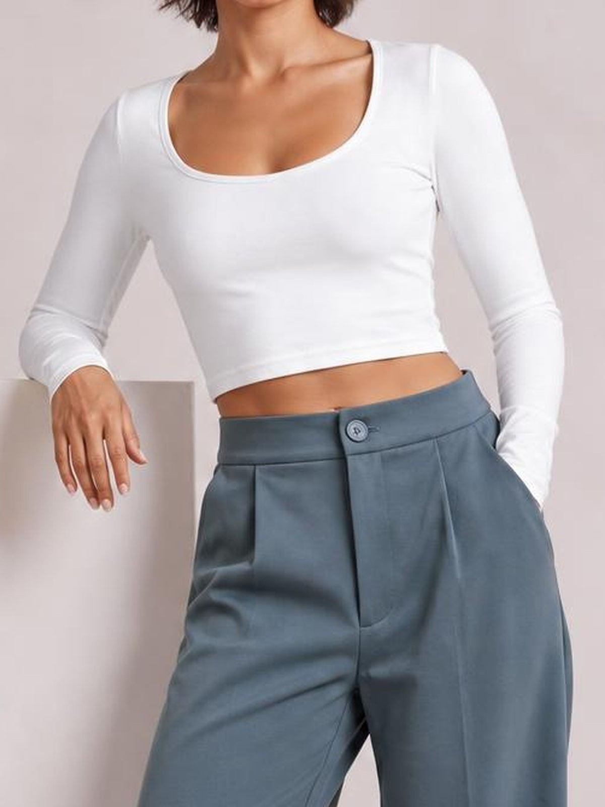 A model poses in blue-gray high waist wide leg pleated pants with a button closure, front pleats, and visible side pockets.