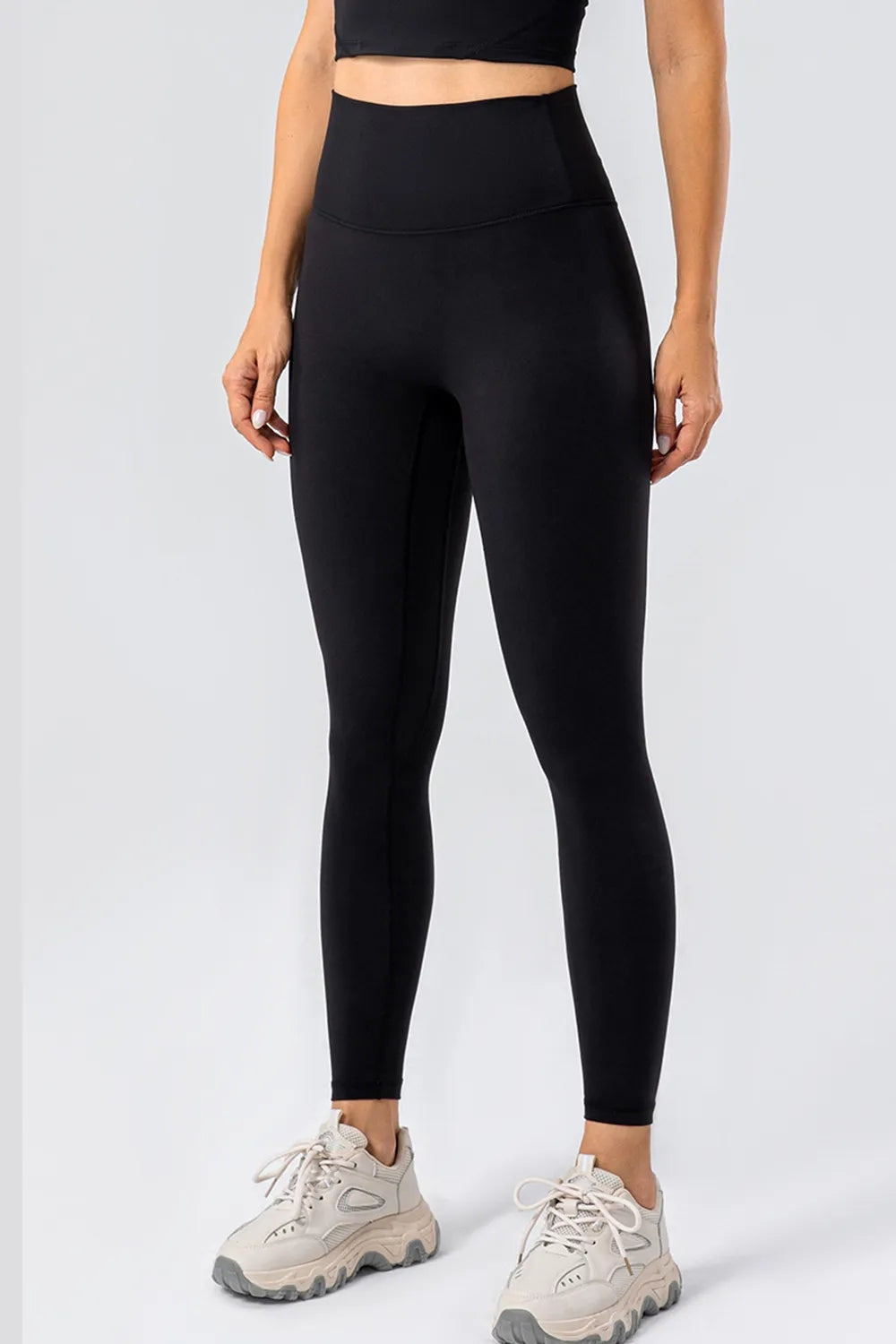 Model stands facing forward in black high-waist active leggings with a wide waistband, sleek fitted silhouette, ankle-length construction, and hands at her sides.