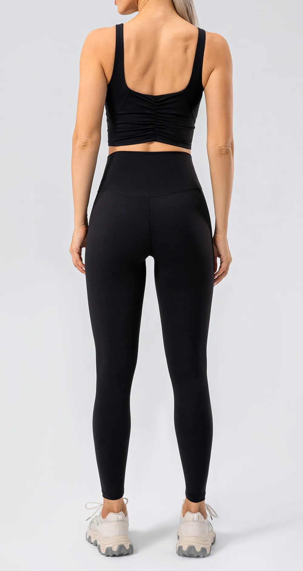 A model stands facing away in black high-waist active leggings with a wide waistband, smooth construction, and a sleek ankle-length fitted silhouette.