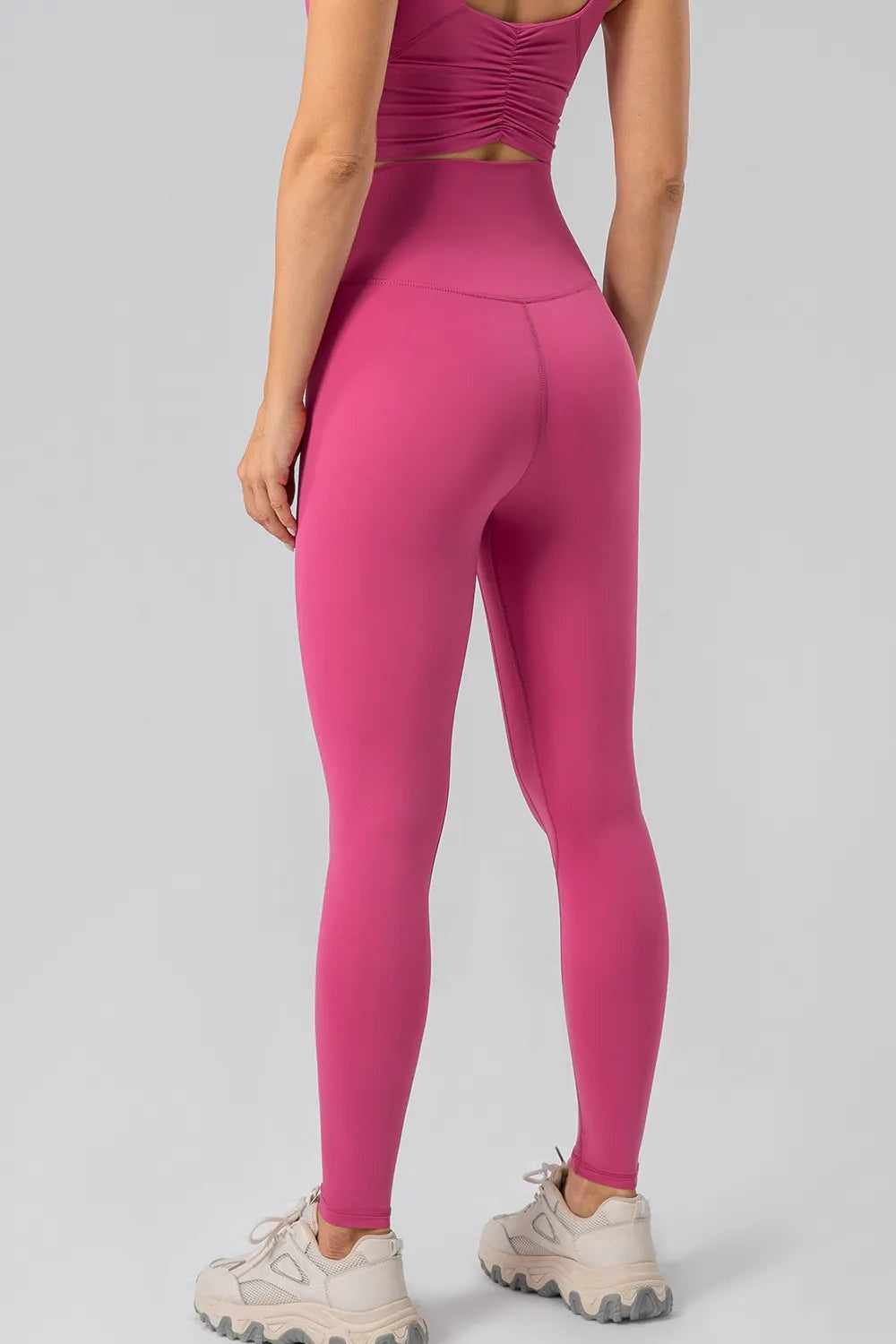 Model shown from behind wearing pink high-waist active leggings with a wide waistband, close-fitting full-length silhouette, and curved seam construction.
