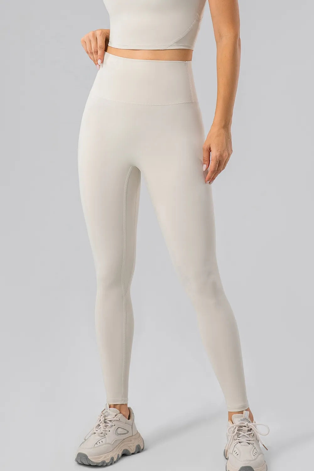 Model in a standing pose wears cream high-waist active leggings with a wide waistband, stretch-fit silhouette, and visible leg seams.