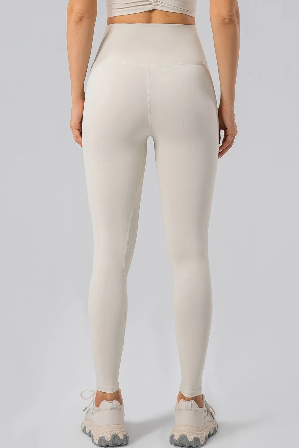 Back view of a standing model wearing cream high-waisted active leggings with a wide waistband, fitted full-length silhouette, and visible center-back seam.