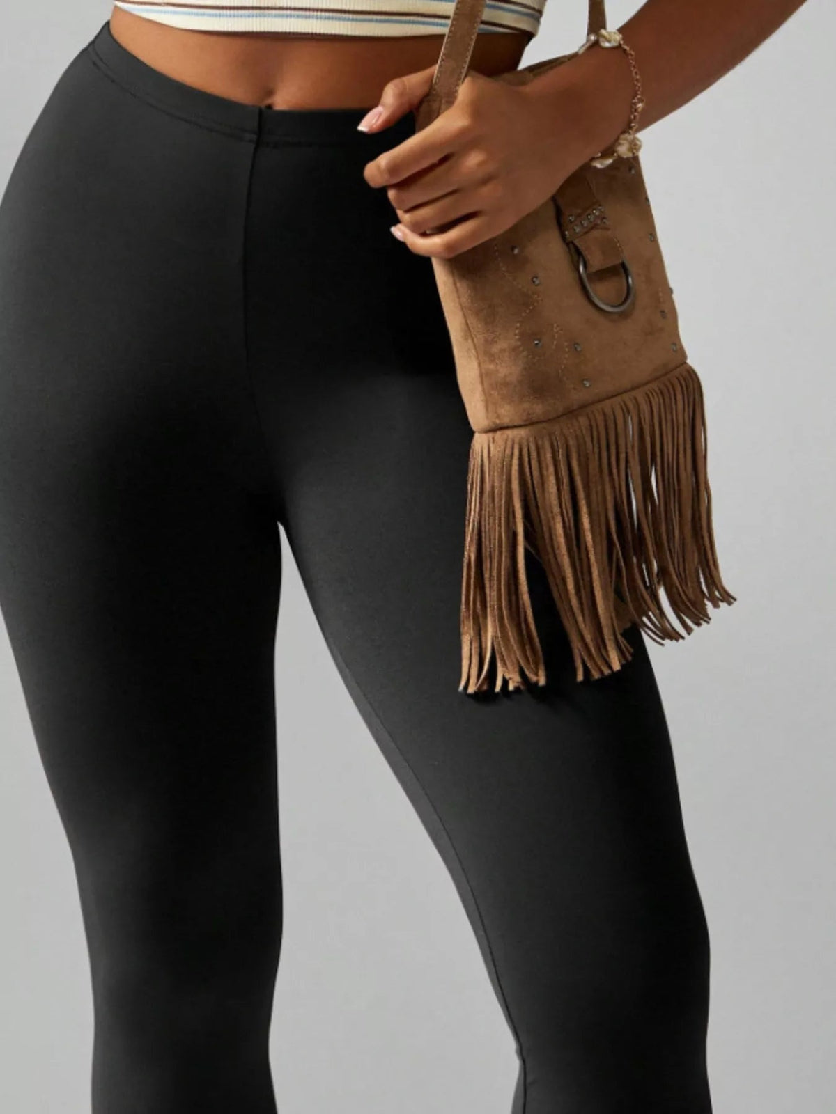 A model wears black high-waisted active leggings with a smooth, close-fitting silhouette and structured waistband, shown in a relaxed standing pose.