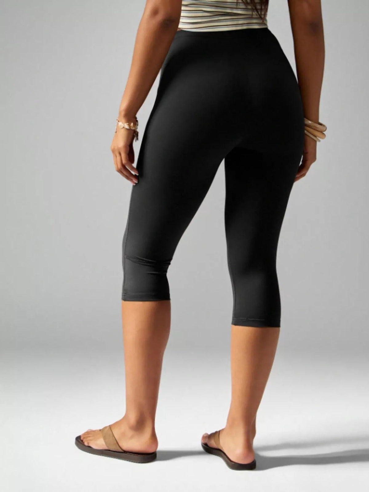 Model shown from behind wearing black high-waisted active capri leggings with a close-fitting silhouette and hemmed knee-length construction.