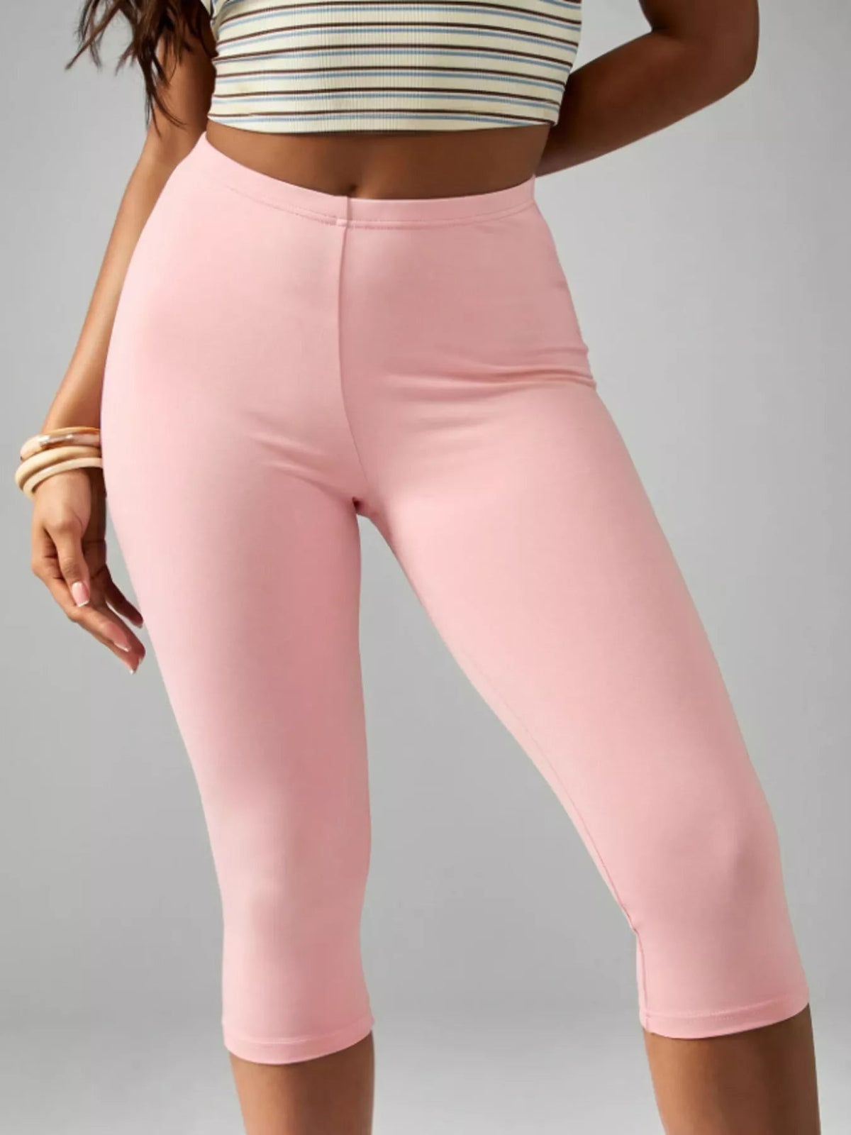 A model poses in pink high-waisted active capri leggings with a smooth fitted silhouette, seamed waistband, and hem below the knees.