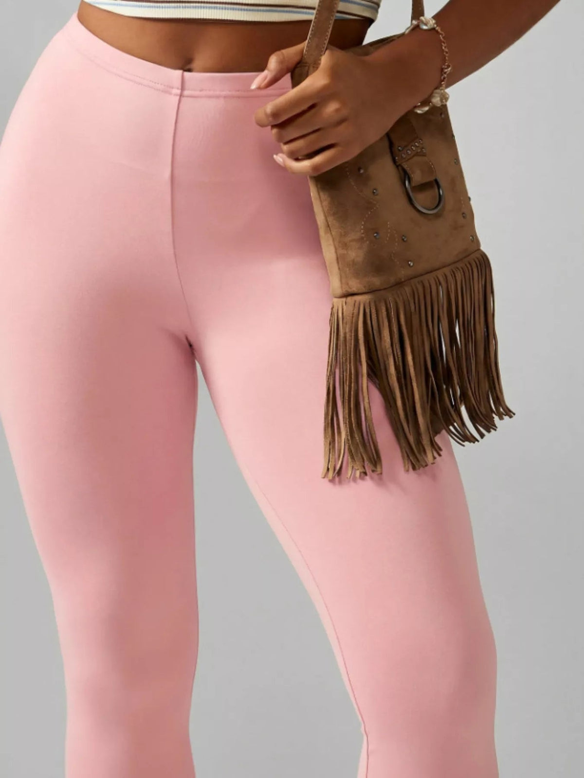 A model wears pink high-waisted active capri leggings with a smooth, fitted silhouette and visible center seam, standing with one hand at the waistband.