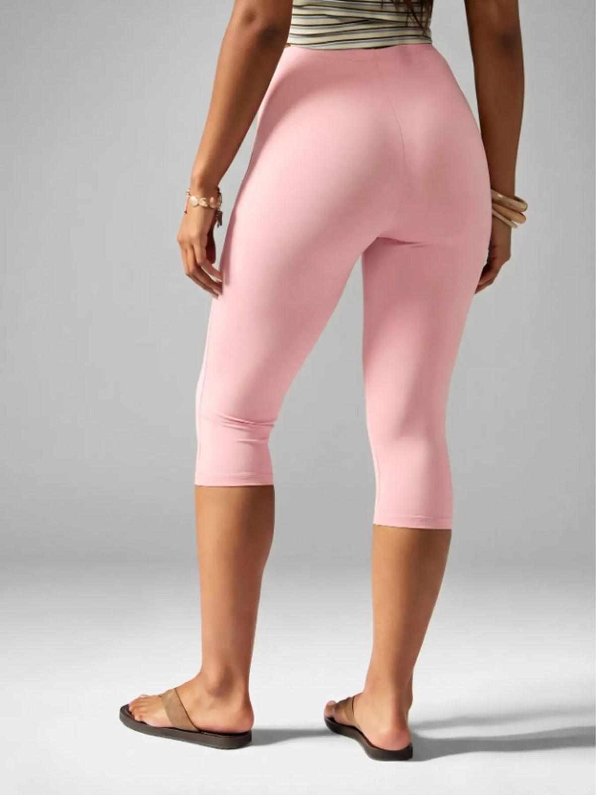 Model shown from behind wearing pink high-waisted active capri leggings with a fitted silhouette, smooth construction, and hems below the knees.