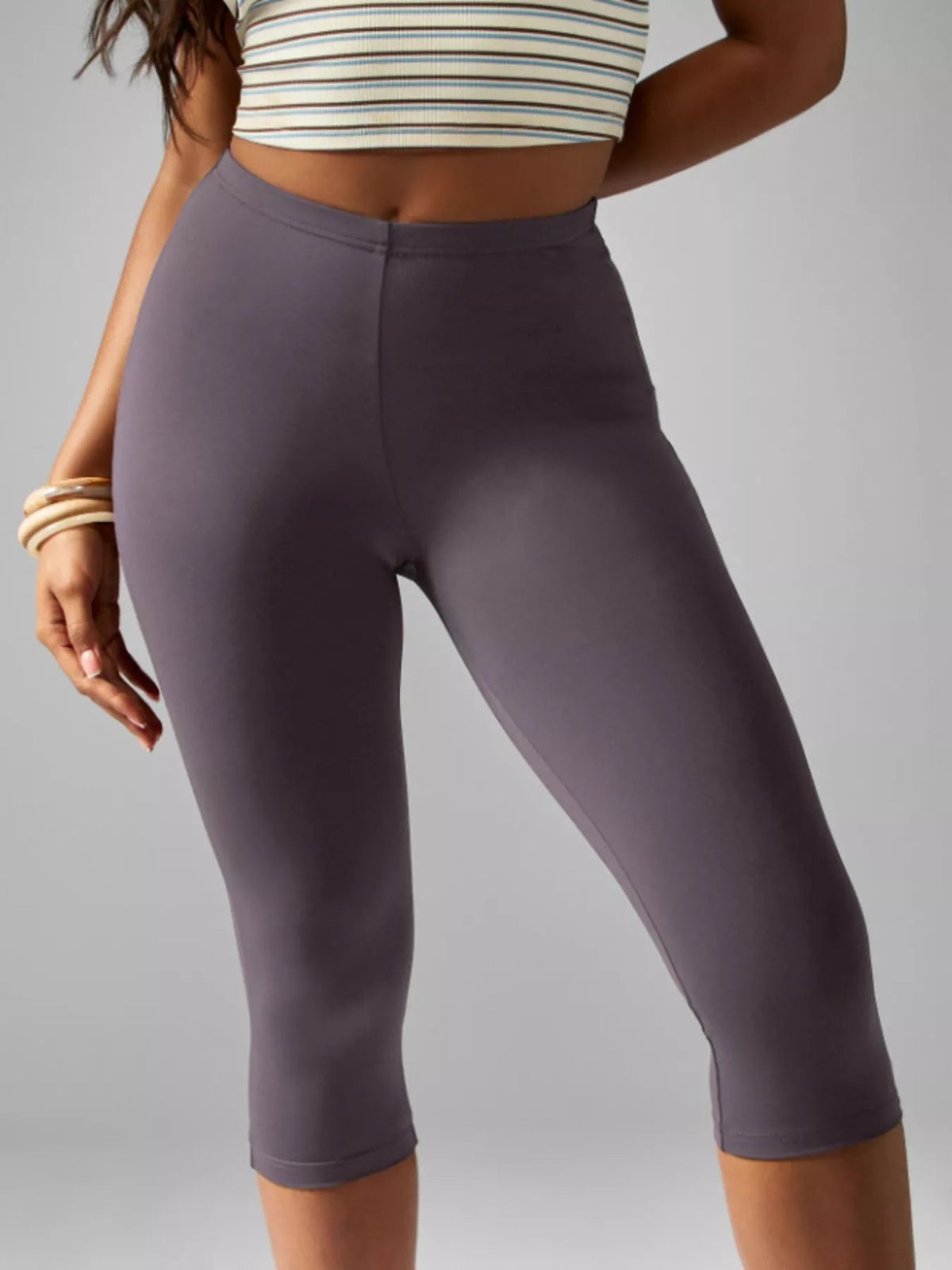 Model poses in dark mauve high-waisted active capri leggings with a smooth, close-fitting silhouette, wide waistband, and stitched hems.