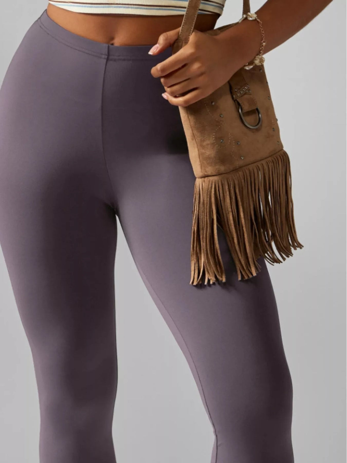 A model wears muted purple high-waisted active leggings with a smooth waistband and sleek, close-fitting silhouette, standing with one hand at her hip.
