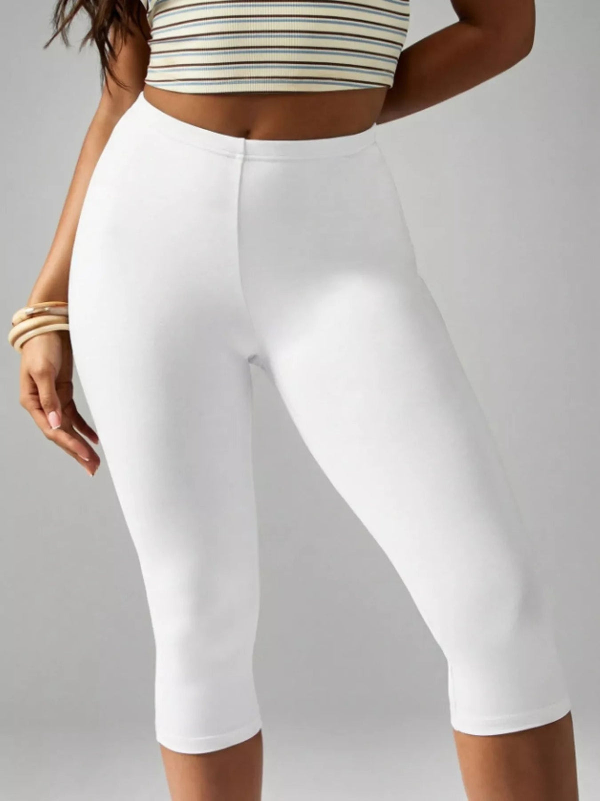 Model poses with one hand at her side, wearing white high-waisted active capri leggings in a smooth, fitted silhouette with clean seamed construction.