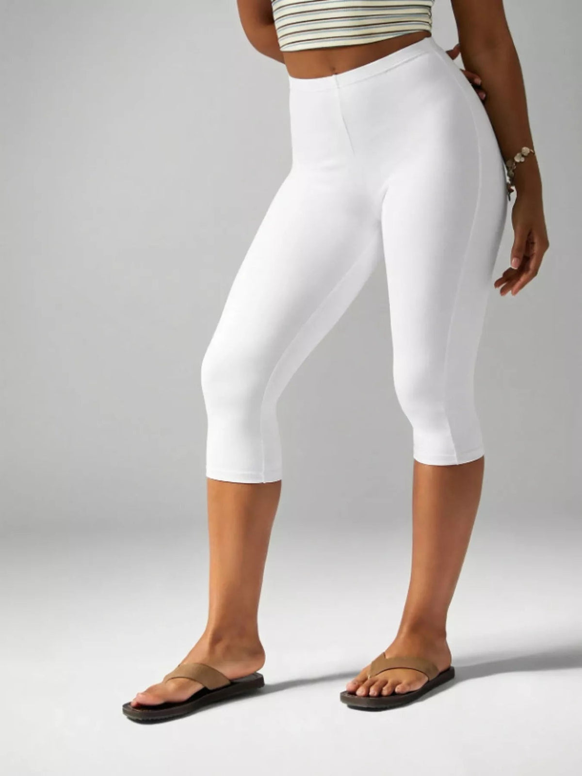 Model wears white high-waisted active capri leggings with a smooth, fitted silhouette, wide waistband, and clean hems, standing with one leg slightly bent.