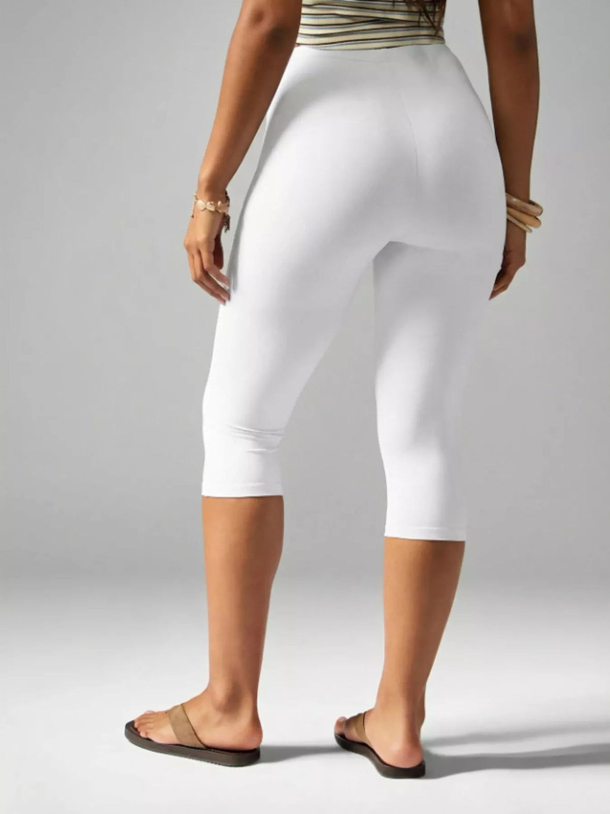 Model shown from behind wearing white high-waisted active capri leggings with a close-fitting silhouette ending below the knees.