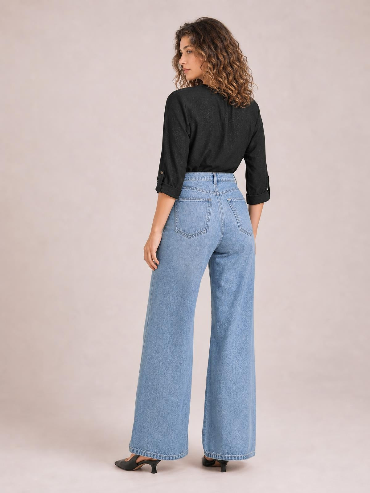 Model poses with her back to the camera, showing light-wash high-waisted bootcut jeans with belt loops, rear pockets, and wide hems.
